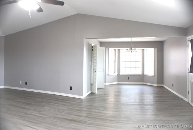 empty room featuring hardwood / wood-style flooring, ceiling fan with notable chandelier, and vaulted ceiling