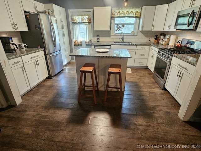 kitchen featuring appliances with stainless steel finishes, white cabinetry, light stone countertops, a center island, and sink