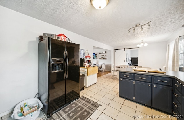 kitchen with a textured ceiling, black fridge with ice dispenser, light tile patterned floors, and a barn door