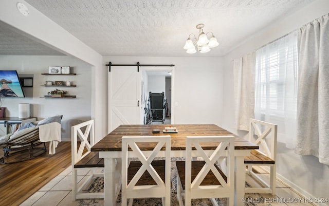 dining room featuring light wood-type flooring, a chandelier, a textured ceiling, and a barn door