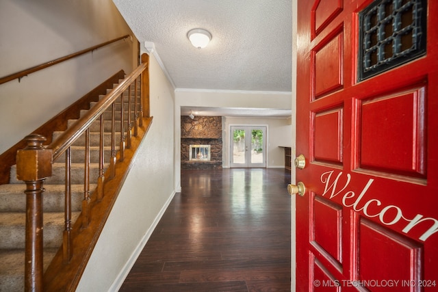 entrance foyer with a textured ceiling, french doors, hardwood / wood-style floors, ornamental molding, and a stone fireplace