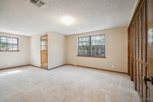 unfurnished bedroom featuring a textured ceiling, a closet, light carpet, and multiple windows