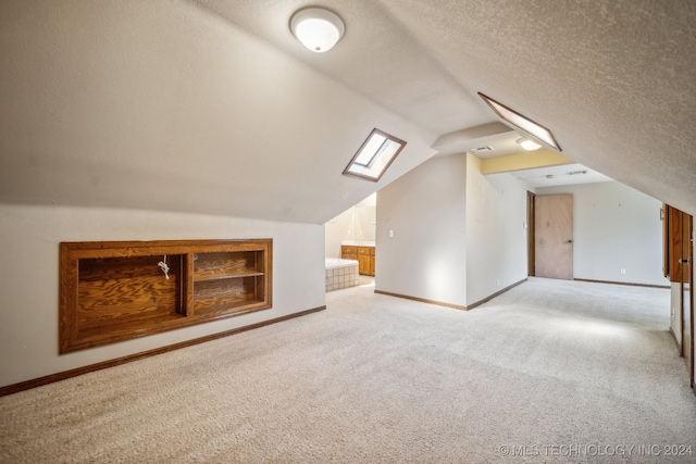 additional living space with built in shelves, light colored carpet, vaulted ceiling with skylight, and a textured ceiling