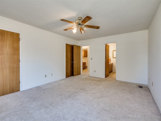 unfurnished bedroom with connected bathroom, light carpet, a textured ceiling, and ceiling fan