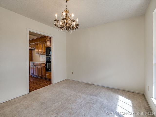 carpeted spare room featuring a notable chandelier and a textured ceiling