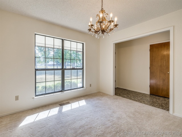 carpeted empty room with a textured ceiling and an inviting chandelier