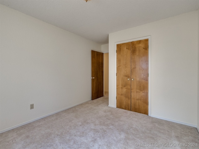 unfurnished bedroom featuring light carpet, a textured ceiling, and a closet