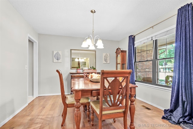 dining room featuring light hardwood / wood-style floors, a textured ceiling, and a notable chandelier