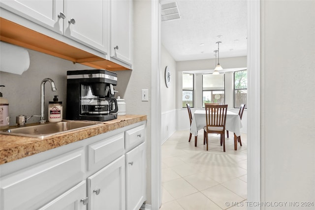 kitchen with light tile patterned flooring, decorative light fixtures, white cabinetry, and sink