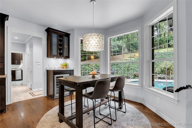 dining space featuring a healthy amount of sunlight, ornamental molding, beverage cooler, and wood-type flooring