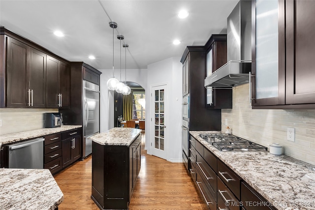 kitchen featuring light wood-type flooring, wall chimney exhaust hood, a center island, and stainless steel appliances