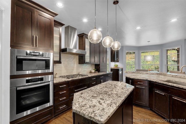 kitchen featuring appliances with stainless steel finishes, hanging light fixtures, wall chimney range hood, and a kitchen island