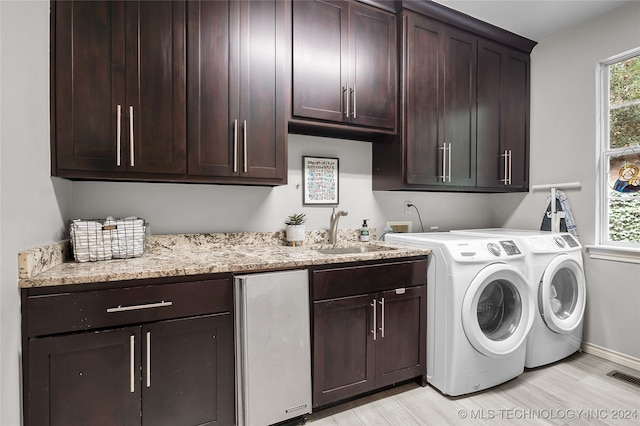 clothes washing area featuring light wood-type flooring, washing machine and dryer, sink, and cabinets