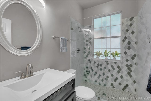 bathroom featuring a tile shower, vanity, and toilet