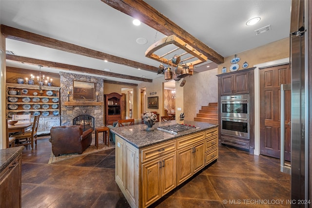 kitchen with dark stone counters, stainless steel appliances, beamed ceiling, a center island, and a stone fireplace