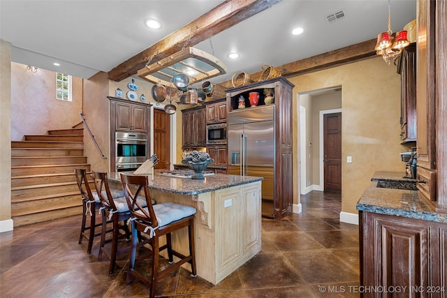 kitchen featuring beam ceiling, a notable chandelier, built in appliances, a kitchen bar, and a kitchen island