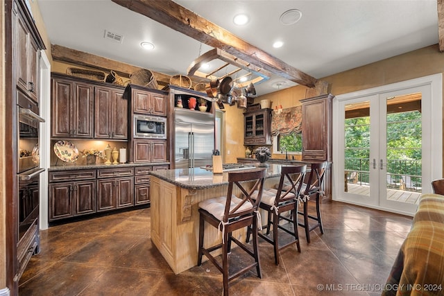 kitchen with a kitchen breakfast bar, beamed ceiling, built in appliances, dark stone counters, and a kitchen island