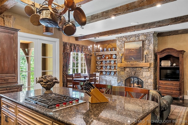 kitchen with beam ceiling, a stone fireplace, stainless steel gas stovetop, and dark stone counters