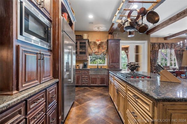 kitchen featuring a center island, dark stone counters, an inviting chandelier, built in appliances, and beam ceiling