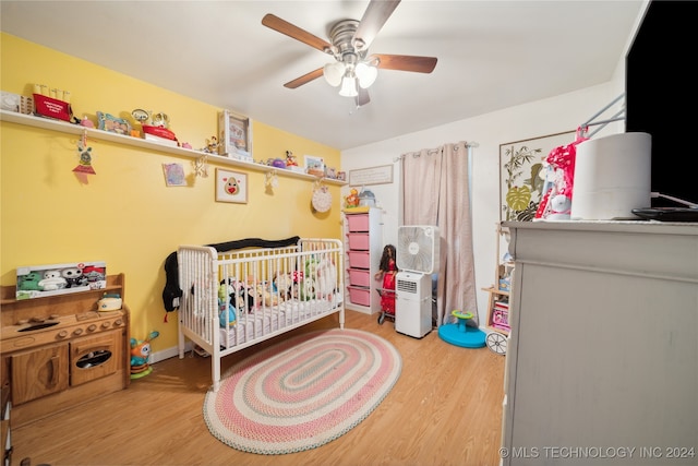 bedroom with ceiling fan, hardwood / wood-style flooring, and a nursery area