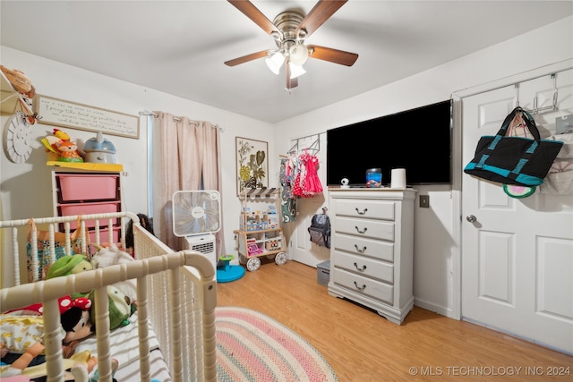 bedroom featuring light hardwood / wood-style floors, a crib, and ceiling fan