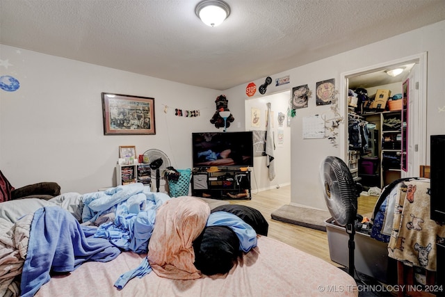 bedroom with a spacious closet, light hardwood / wood-style floors, and a textured ceiling