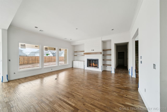 unfurnished living room featuring built in shelves, dark hardwood / wood-style floors, and ornamental molding