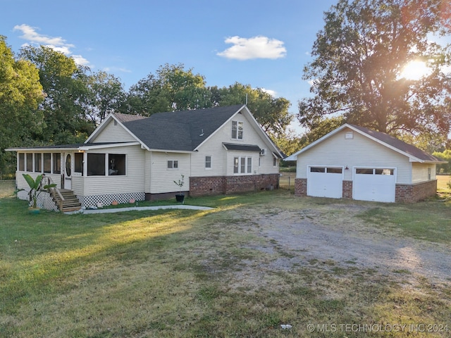 view of front of property featuring a garage, a sunroom, a front lawn, and an outbuilding