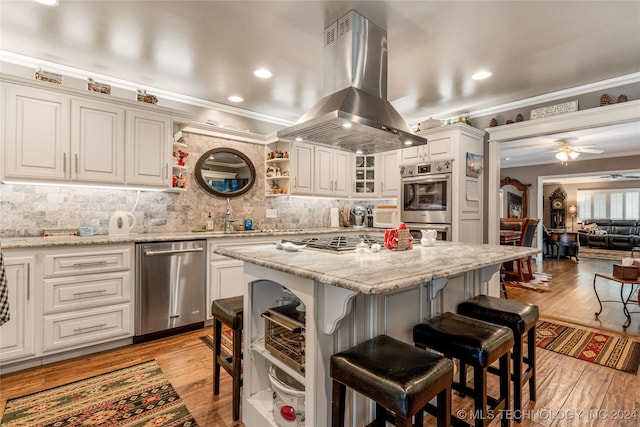 kitchen featuring light hardwood / wood-style floors, island range hood, stainless steel appliances, crown molding, and ceiling fan