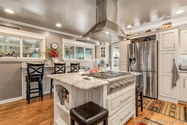 kitchen featuring light wood-type flooring, a center island, ventilation hood, a kitchen bar, and appliances with stainless steel finishes