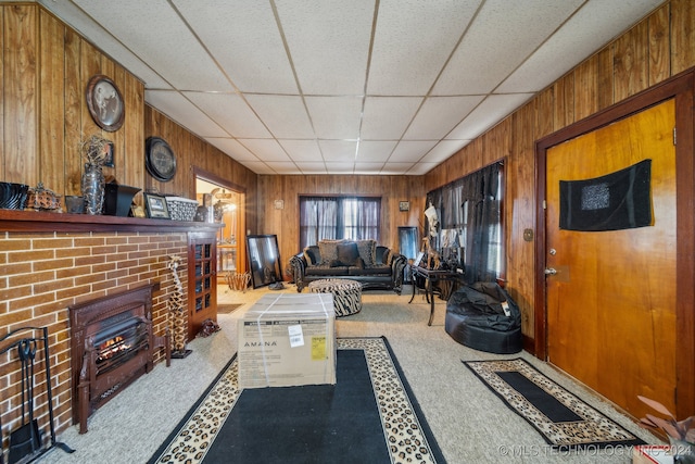 living room with wood walls, a drop ceiling, and a brick fireplace