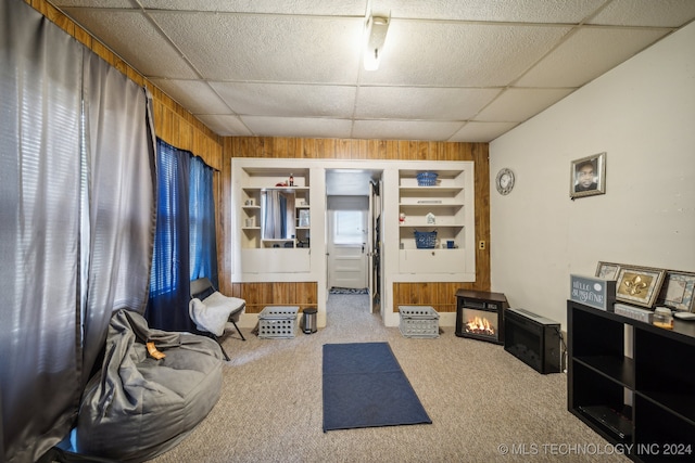 sitting room with wooden walls, a drop ceiling, light colored carpet, and a wood stove