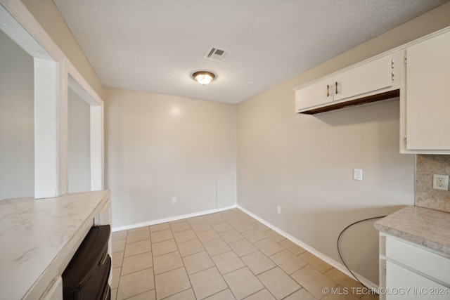 kitchen featuring a textured ceiling, light tile patterned flooring, and white cabinetry