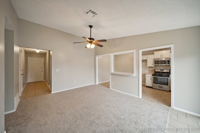 empty room with a textured ceiling, vaulted ceiling, light carpet, and ceiling fan