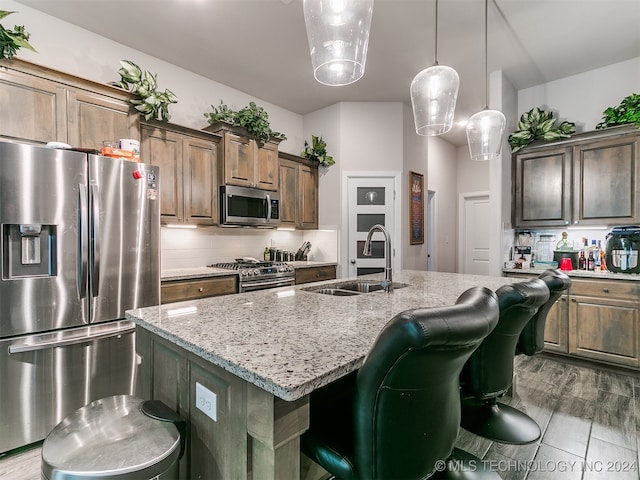 kitchen featuring light stone countertops, a center island with sink, appliances with stainless steel finishes, and sink