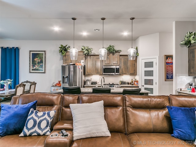 kitchen featuring stainless steel appliances, a center island with sink, a kitchen bar, and decorative light fixtures