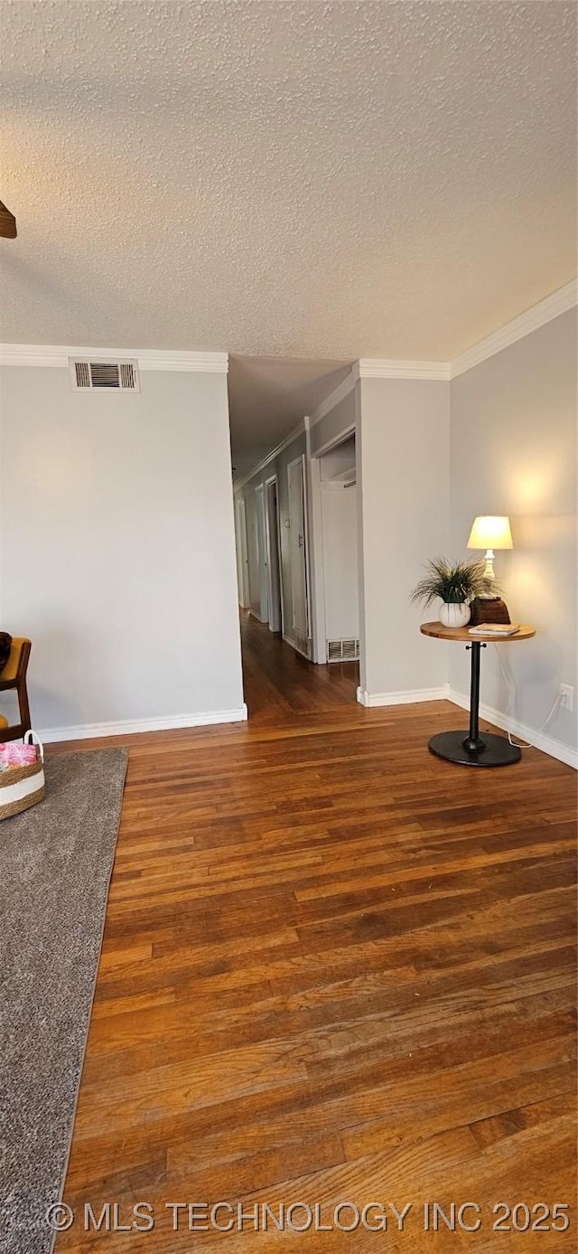 empty room with a textured ceiling, dark hardwood / wood-style floors, and ornamental molding