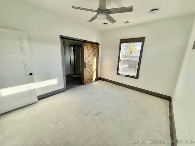 unfurnished bedroom with concrete flooring, a barn door, and ceiling fan