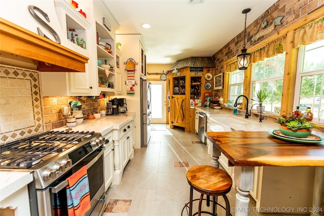 kitchen featuring a breakfast bar, white cabinets, hanging light fixtures, stainless steel appliances, and light stone countertops