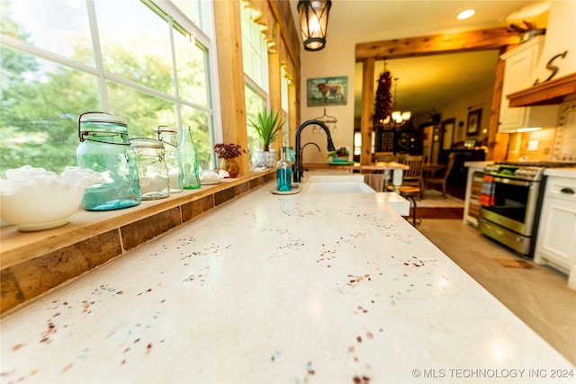 kitchen with stainless steel range, white cabinetry, sink, and a notable chandelier