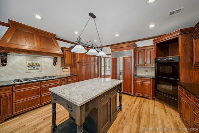 kitchen with stainless steel gas cooktop, a kitchen island, decorative light fixtures, crown molding, and light hardwood / wood-style floors