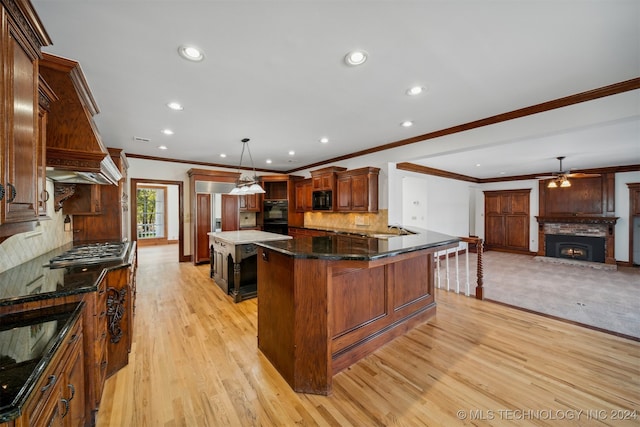 kitchen featuring a kitchen breakfast bar, a stone fireplace, pendant lighting, light wood-type flooring, and ceiling fan