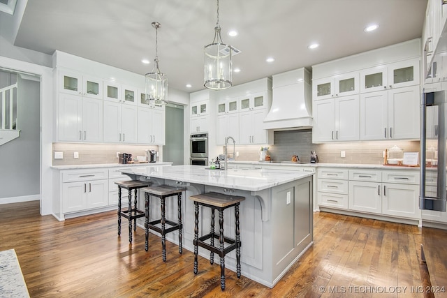 kitchen featuring custom range hood, a kitchen island with sink, dark hardwood / wood-style floors, and white cabinets