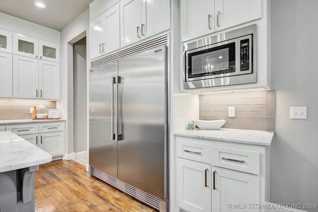 kitchen featuring light stone counters, white cabinets, light hardwood / wood-style flooring, backsplash, and built in appliances