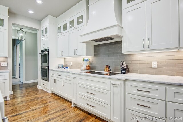 kitchen featuring black electric cooktop, light hardwood / wood-style flooring, custom range hood, and white cabinetry