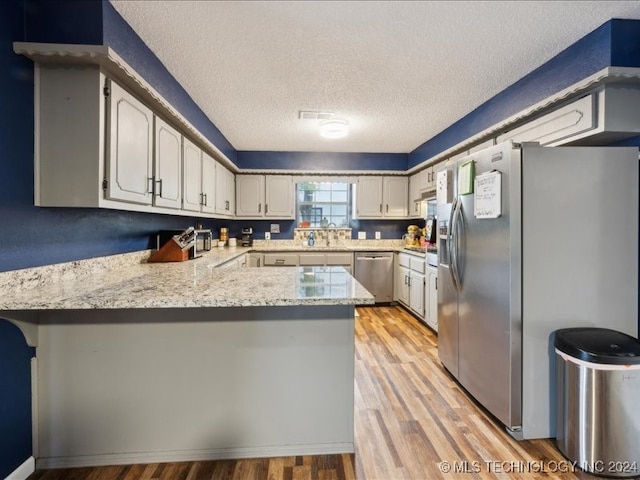 kitchen with appliances with stainless steel finishes, a textured ceiling, light hardwood / wood-style floors, and kitchen peninsula