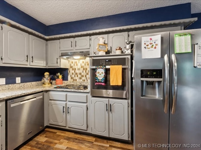 kitchen with a textured ceiling, dark wood-type flooring, white cabinetry, decorative backsplash, and appliances with stainless steel finishes