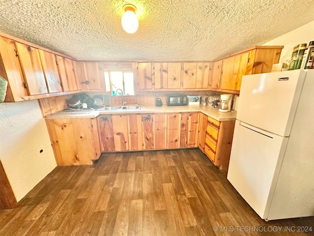 kitchen featuring dark wood-type flooring, white refrigerator, a textured ceiling, light brown cabinetry, and sink