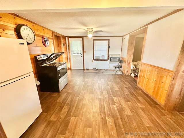 kitchen featuring white refrigerator, stainless steel range oven, ceiling fan, wooden walls, and hardwood / wood-style floors