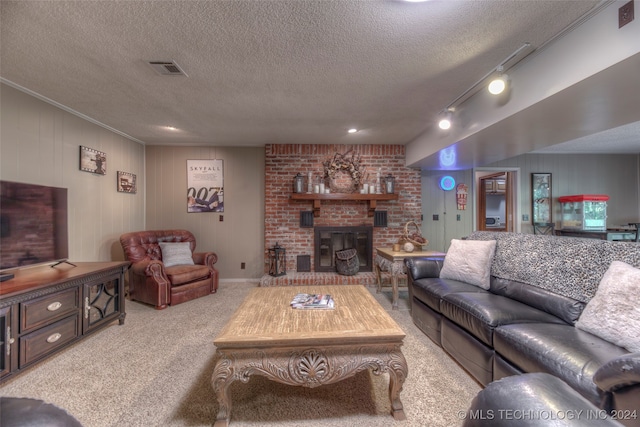 living room with wood walls, a brick fireplace, a textured ceiling, track lighting, and light carpet